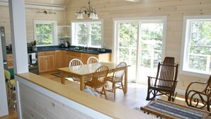 A wooden interior with a kitchen, dining area, and large windows. - Tranquil oceanfront cottage on Wohoa Bay (Addison)
