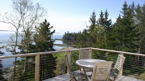 A wooden deck with a table and chairs overlooking a body of water and forested area. - Tranquil oceanfront cottage on Wohoa Bay (Addison)