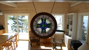 A cozy room with a wooden interior, a round stained glass window, a dining table with chairs, and a bookshelf. - Tranquil oceanfront cottage on Wohoa Bay (Addison)