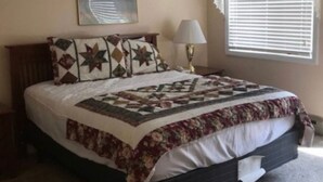 Ein Schlafzimmer mit einem Bett, einem Nachttisch, einer Lampe, einem Fenster mit Jalousien und einem Deckenventilator.
