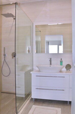 Une salle de bain moderne avec une douche à parois de verre, un lavabo blanc et un grand miroir au-dessus du meuble-lavabo.