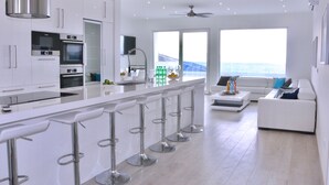Una cucina moderna con isola centrale, sgabelli da bar e vista sull'oceano attraverso ampie finestre.