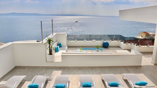 Una terrazza sul tetto con lettini e una piscina, con vista su un lago e montagne lontane.