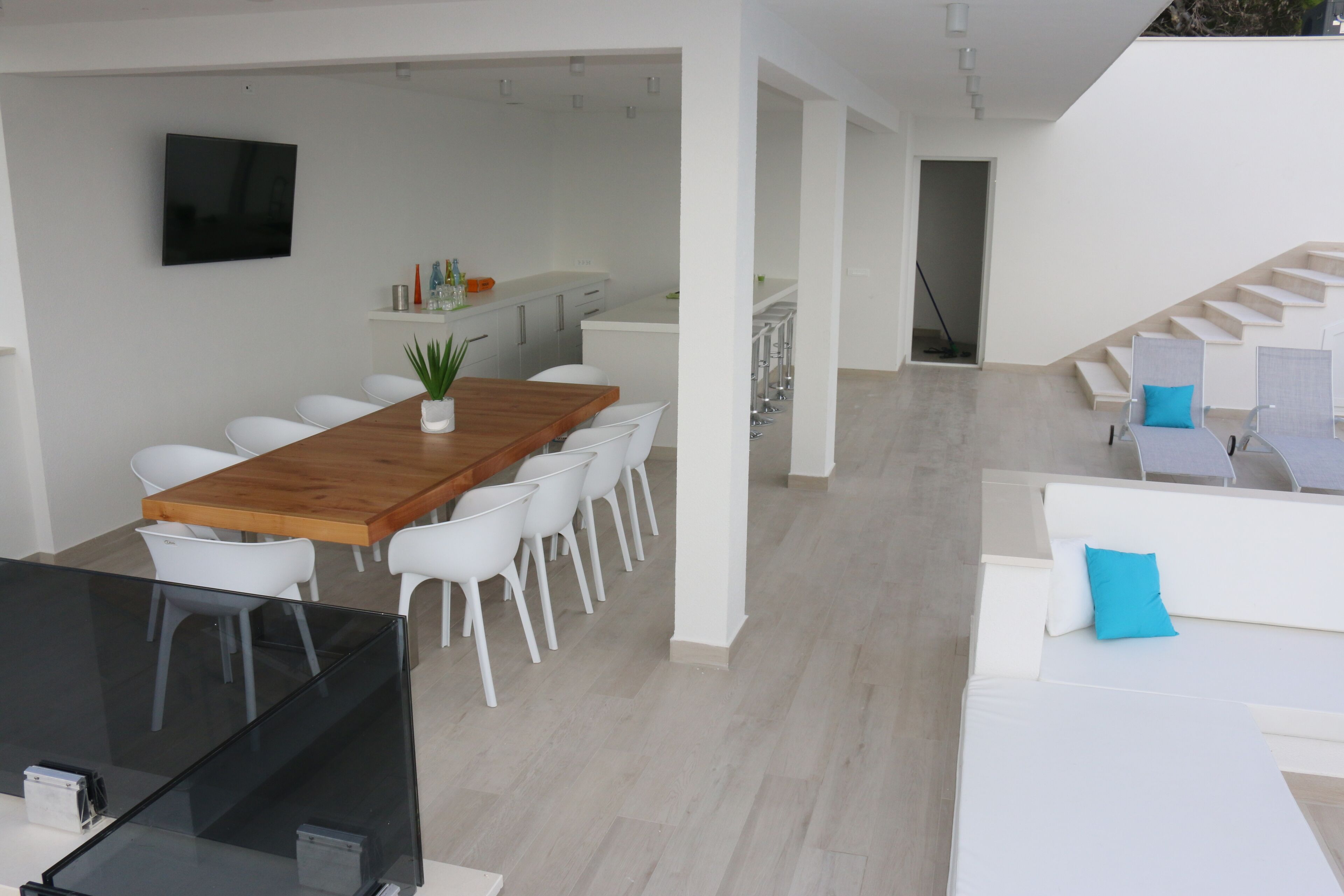 Un intérieur moderne avec une table à manger en bois, des chaises blanches, une table en verre noir et un canapé blanc agrémenté de coussins bleus.