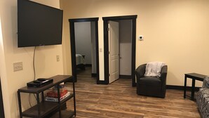 A living room with a flat-screen TV, a console table with electronics, a leather sofa, and a patterned armchair. - Rider’s Rest # 2 within 2 miles of Tryon International Equestrian Center (Rutherfordton)