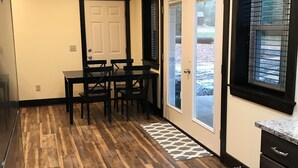 A kitchen with wooden flooring, a dining table with chairs, a refrigerator, and a window with blinds. - Rider’s Rest # 2 within 2 miles of Tryon International Equestrian Center (Rutherfordton)