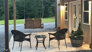 A covered porch with a swing set, two wicker chairs, a small table, and a potted plant. - Rider’s Rest # 2 within 2 miles of Tryon International Equestrian Center (Rutherfordton)