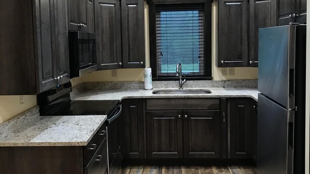 A kitchen with dark wooden cabinets, a granite countertop, a stainless steel refrigerator, and a window with blinds. - Rider’s Rest # 2 within 2 miles of Tryon International Equestrian Center (Rutherfordton)