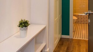 Un couloir avec un banc blanc, une plante en pot, un mur d’accent de couleur turquoise et une porte donnant sur une salle de bain aux carreaux décorés.