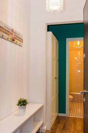 Ein Flur mit einer weißen Bank, einem Blumentopf, einer türkisfarbenen Akzentwand und einer Tür zu einem Badezimmer mit Musterfliesen.