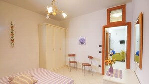 Une chambre à coucher comprenant un lit, deux chaises, un bureau avec un vase de fleurs, une armoire et un miroir.
