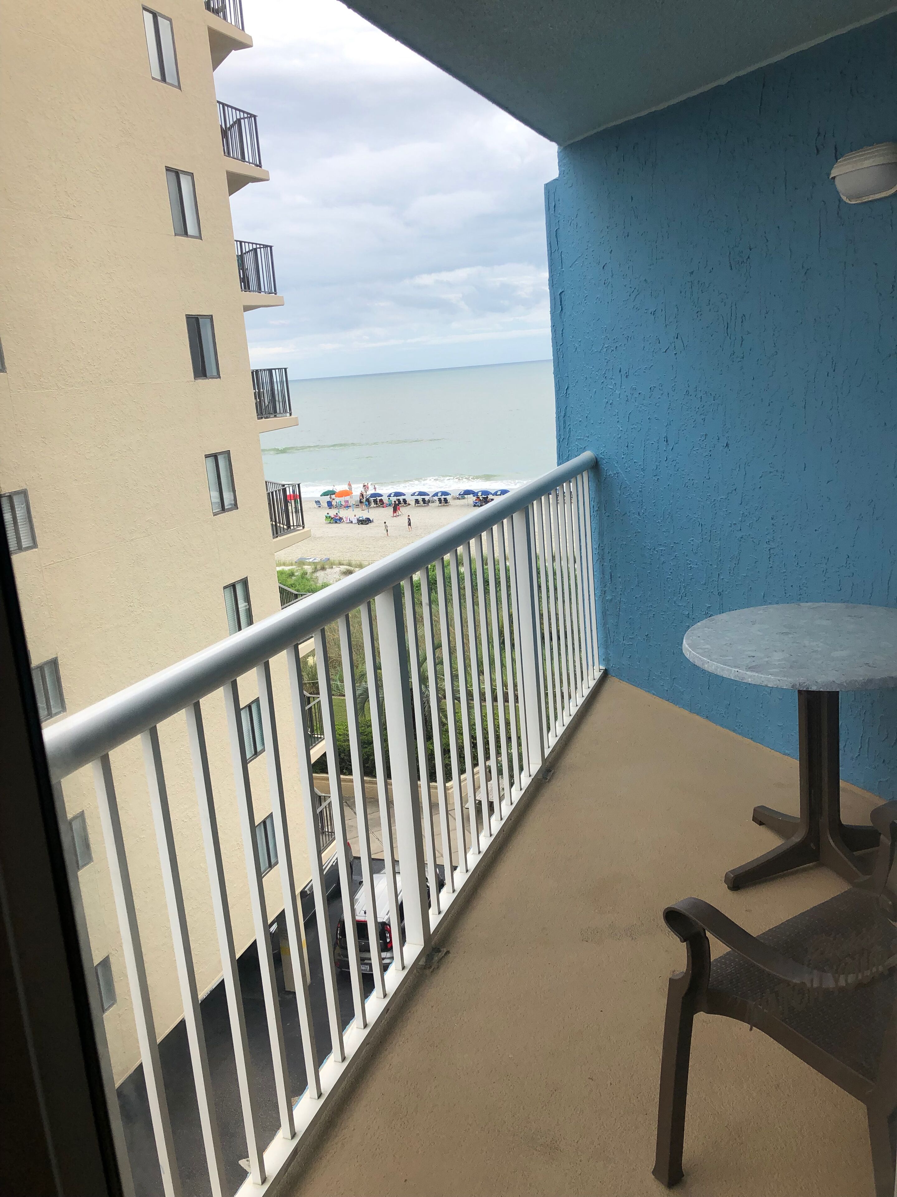 A balcony with a view of a beach, a table, and a railing.