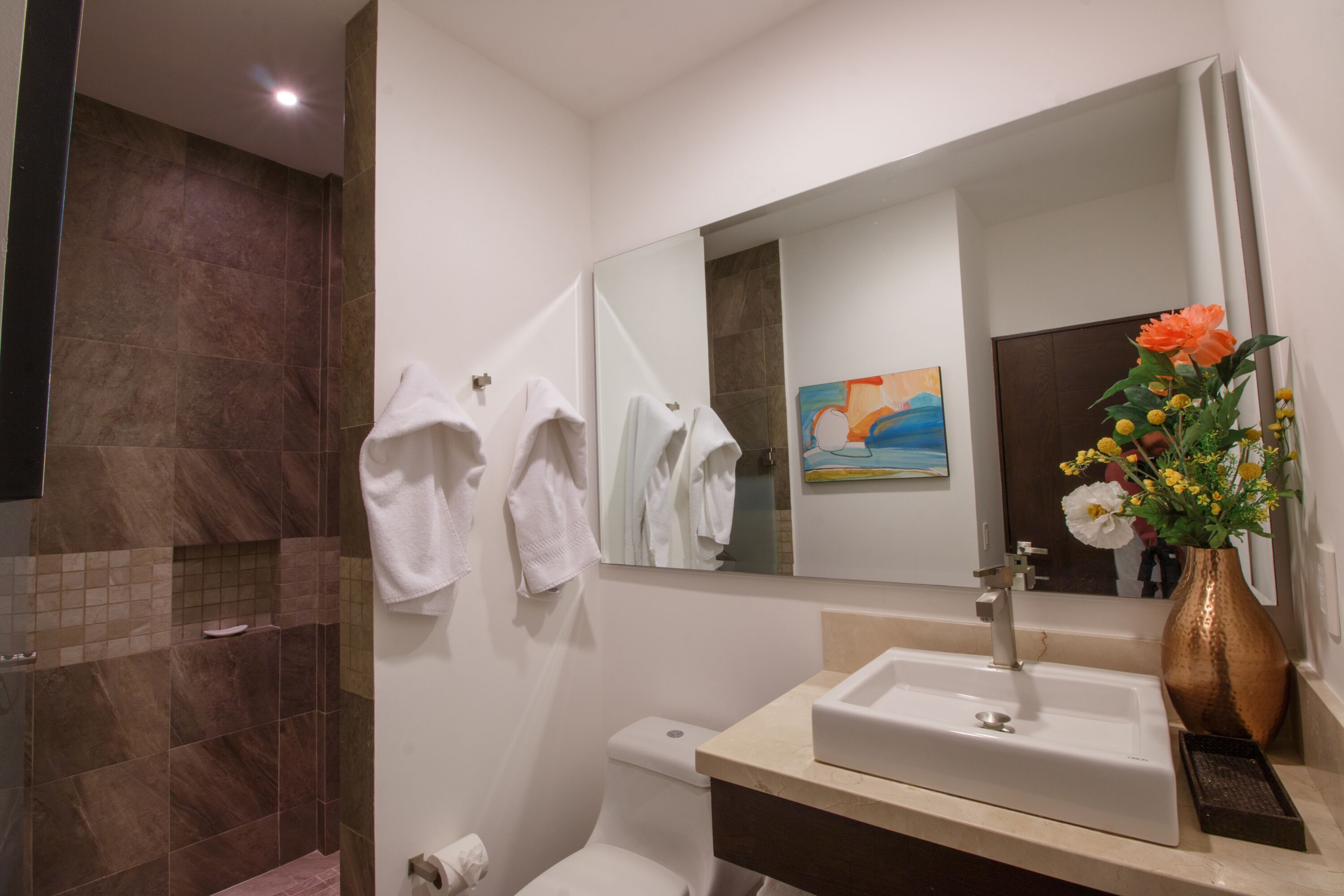 A bathroom with a shower, toilet, sink, and a large mirror.
