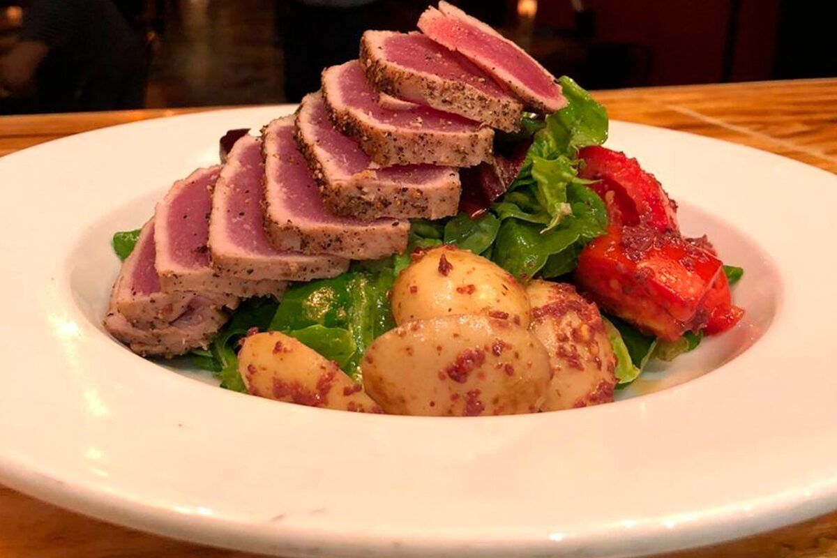 Une assiette de nourriture composée de viande en tranches, de pommes de terre et de légumes verts.