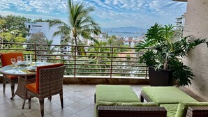 Een balkon met rieten meubilair, een eettafel en een grote potplant.