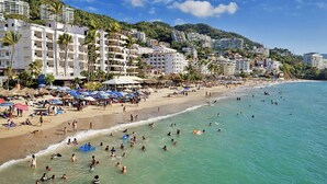 Een strand met mensen die zwemmen en zonnebaden, omringd door meer verdiepingen tellende gebouwen en palmbomen.