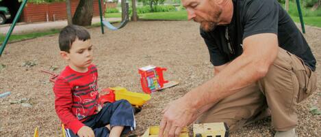 A man and a child playing with toy vehicles on a gravel surface.