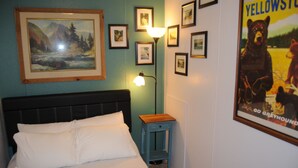 Een slaapkamer met een bed, nachtkastje, lamp, ingelijste foto’s aan de muur en een poster met beren.