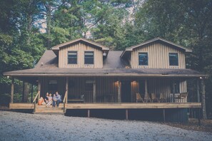 A two-story wooden cabin with a porch, surrounded by trees. - Oxford Retreat - 4B/4B Newly Renovated Cabin 15 Minutes From Downtown Oxford! (Batesville)