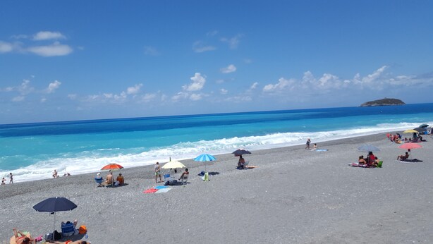 A beach with people sunbathing and swimming, umbrellas, and a distant island. - DIAMOND - ITALY - SUN AND SEA (Diamante)