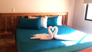 Un letto con biancheria color turchese, una testiera in legno e un'accogliente composizione di asciugamani a forma di cuore.