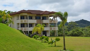 Un edificio a più piani con tetto piatto, immerso in un paesaggio verdeggiante e palme.