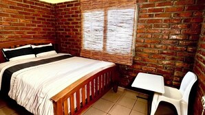 Una habitación con pared de ladrillo, una cama con cabecera de madera, una mesita y una silla blanca.