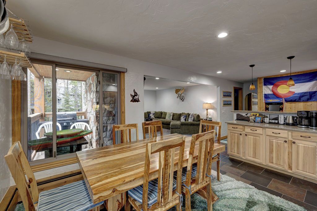 A dining area with a wooden table and chairs, a kitchen with light wooden cabinets, and a view of the outdoors through a sliding glass door.