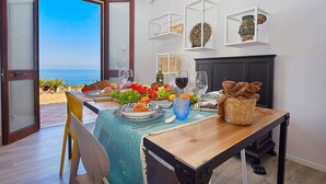 A dining area with a table set for a meal, a view of the sea through an open door, and decorative items on the wall. - VILLA TARI' (Scopello)