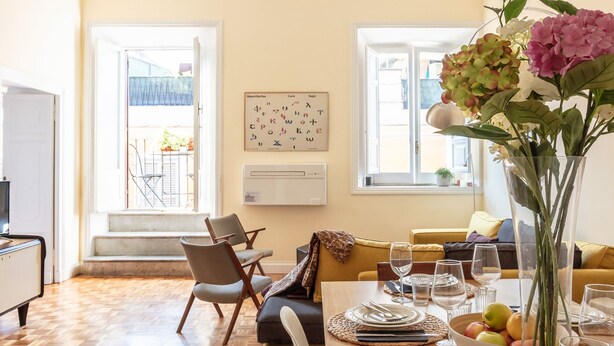 A dining area with a wooden table set for four, a vase with flowers, and a view of the outside balcony.