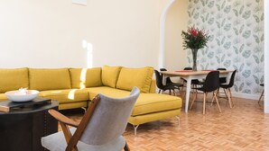 A modern living room with a yellow sofa, a round coffee table, and a dining area with a table and chairs.