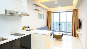 A modern kitchen with a built-in stove, a dining area with a table and chairs, and a large window with curtains. - Lovina Residences at Harbour Bay (Batam)