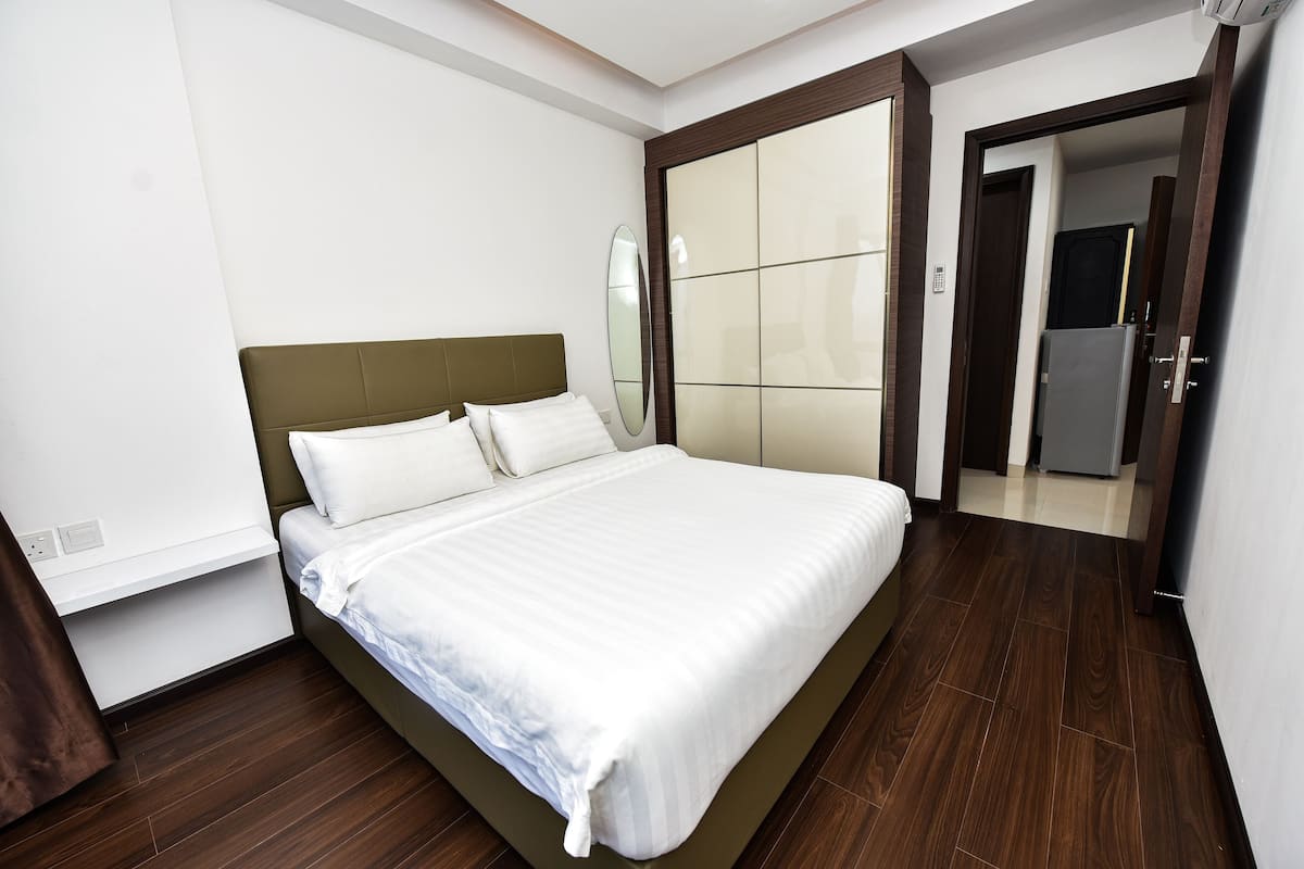 Ein ordentlich bezogenes Bett in einem Hotelzimmer mit Holzboden, einem großen Spiegel und einer Tür zu einem weiteren Raum.
