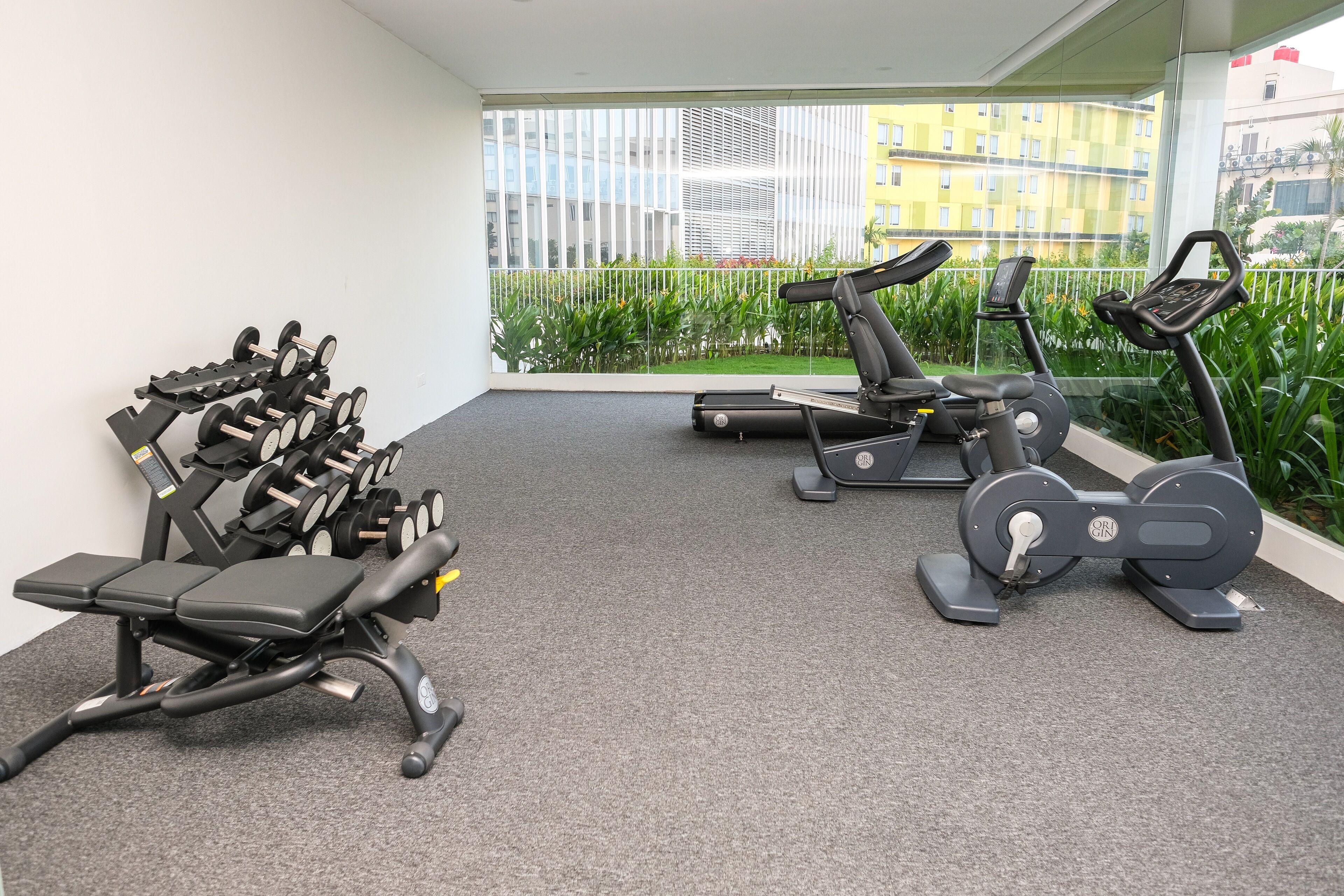 A gym with various exercise equipment including dumbbells, a bench, and treadmills.