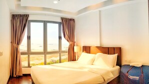 A hotel room with a large window, a bed, a nightstand, and a suitcase. - Lovina Residences at Harbour Bay (Batam)