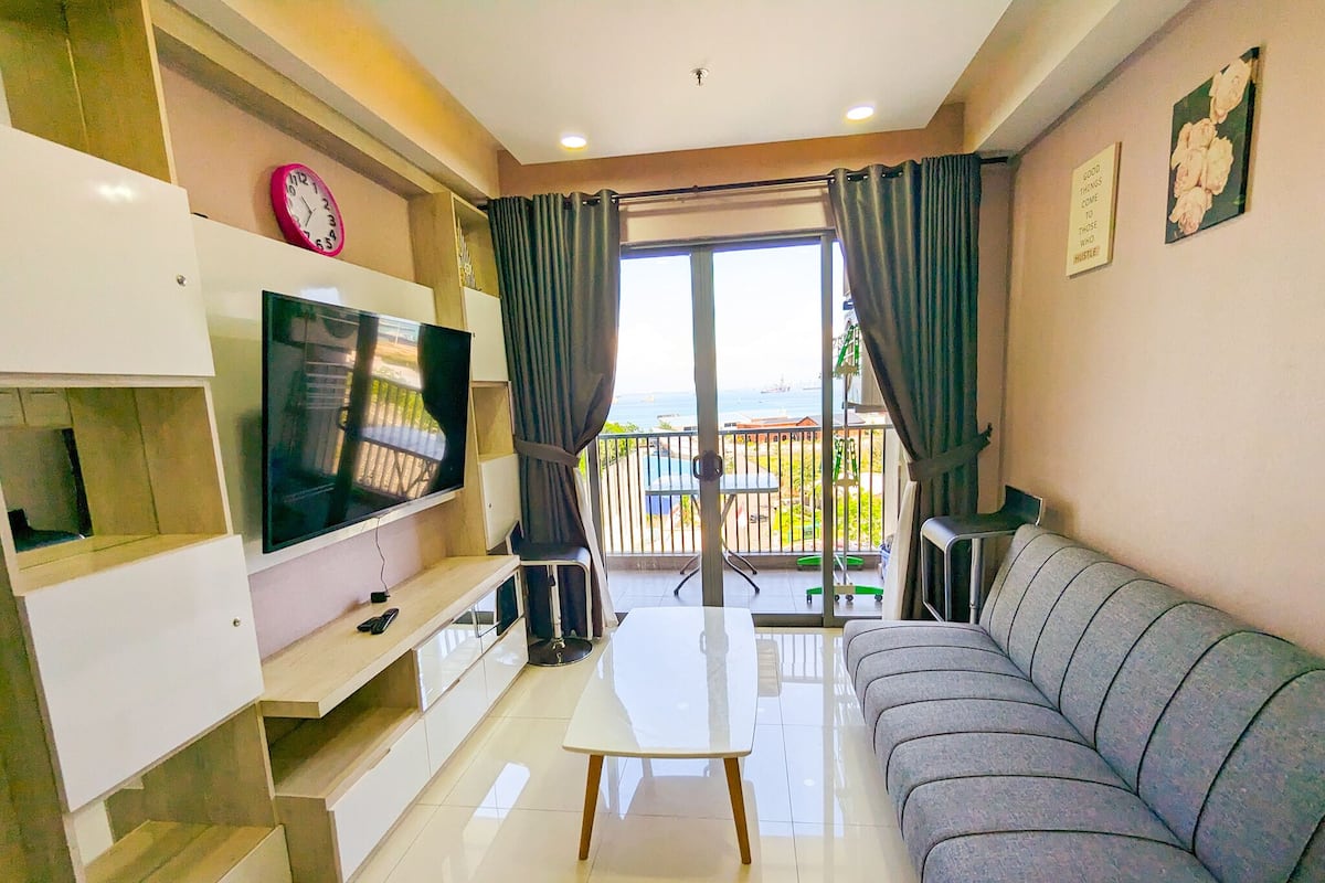 Ein modernes Wohnzimmer mit Flachbildfernseher, einer Couch, einem Couchtisch und einem Balkon mit Blick.