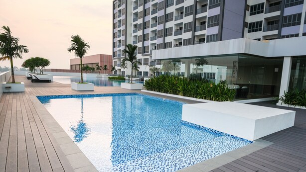 A modern hotel with a rooftop pool, surrounded by palm trees and a high-rise building in the background. - Lovina Residences at Harbour Bay (Batam)