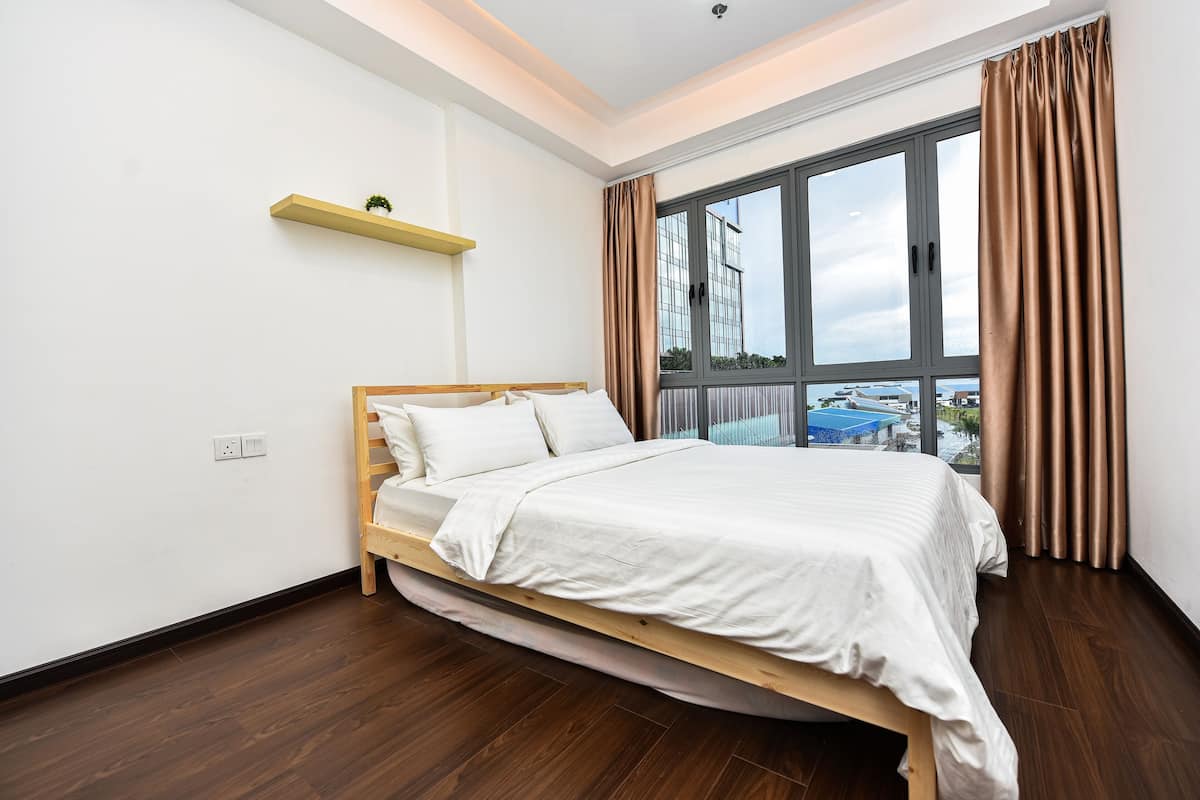 Ein modernes Schlafzimmer mit einem hölzernen Bett, einem Fenster mit Vorhängen und einer kleinen Ablage mit einer Pflanze.