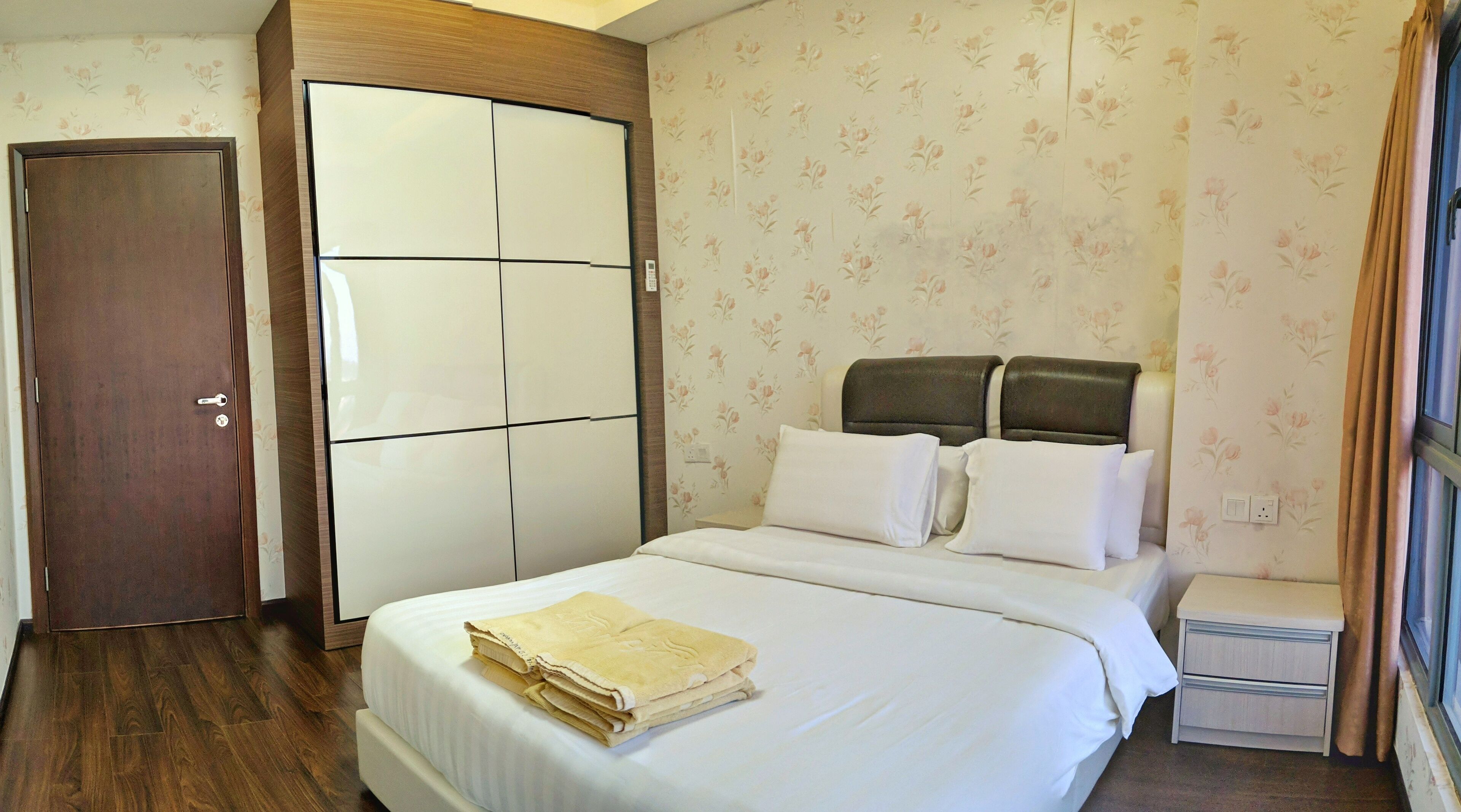A hotel room with a bed, a wardrobe, a nightstand, and a window with curtains.