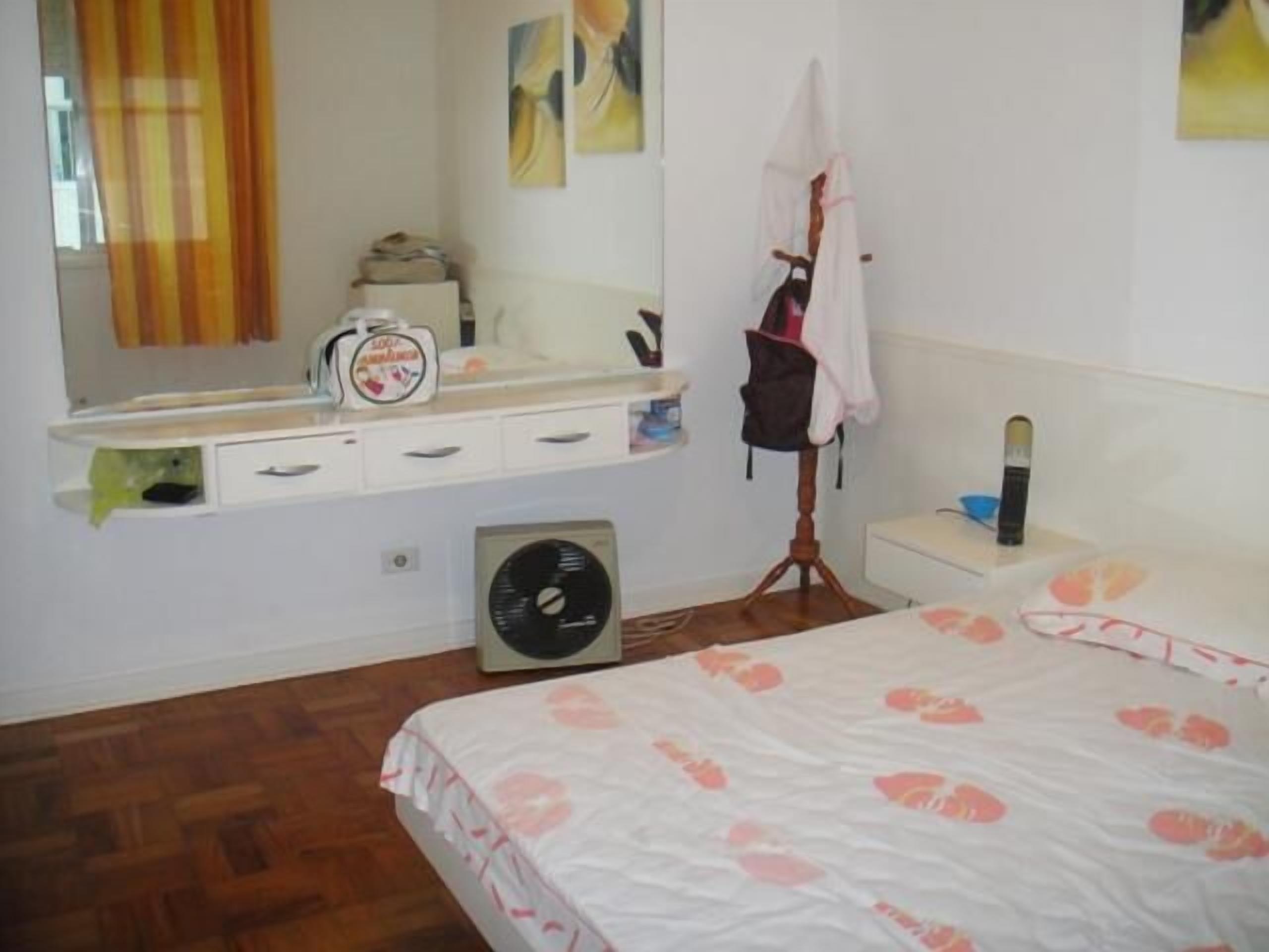 Una camera da letto con un letto, un comodino, uno specchio, una ventola e una finestra con tende.
