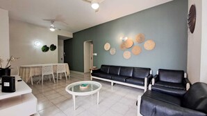 En moderne stue med en sort lædersofa, et glasbord og et spiseområde med et hvidt bord og stole.