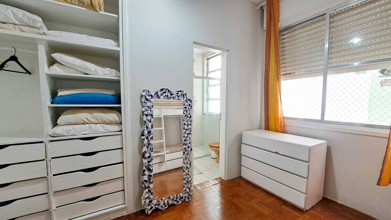 Ein Schlafzimmer mit begehbarem Kleiderschrank, einem Schminkschrank mit Spiegel und einem Fenster mit Jalousien.
