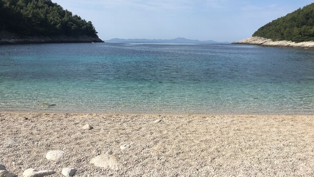 Una playa de guijarros con agua cristalina y montañas a lo lejos.