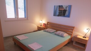 Un dormitorio con una cama individual, dos mesitas de noche, un tocador, una ventana con persianas y un cuadro colgado en la pared.
