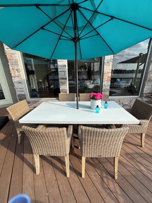 Un patio con una mesa blanca, sillas de mimbre, un parasol turquesa y una pared de piedra.