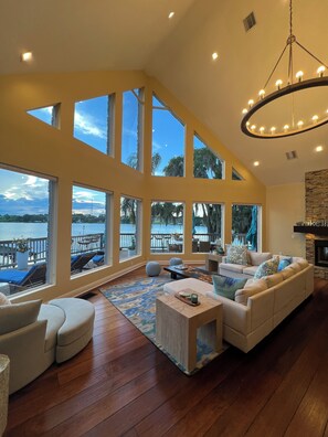 A spacious living room with a large sofa, a coffee table, and a view of the water through large windows.