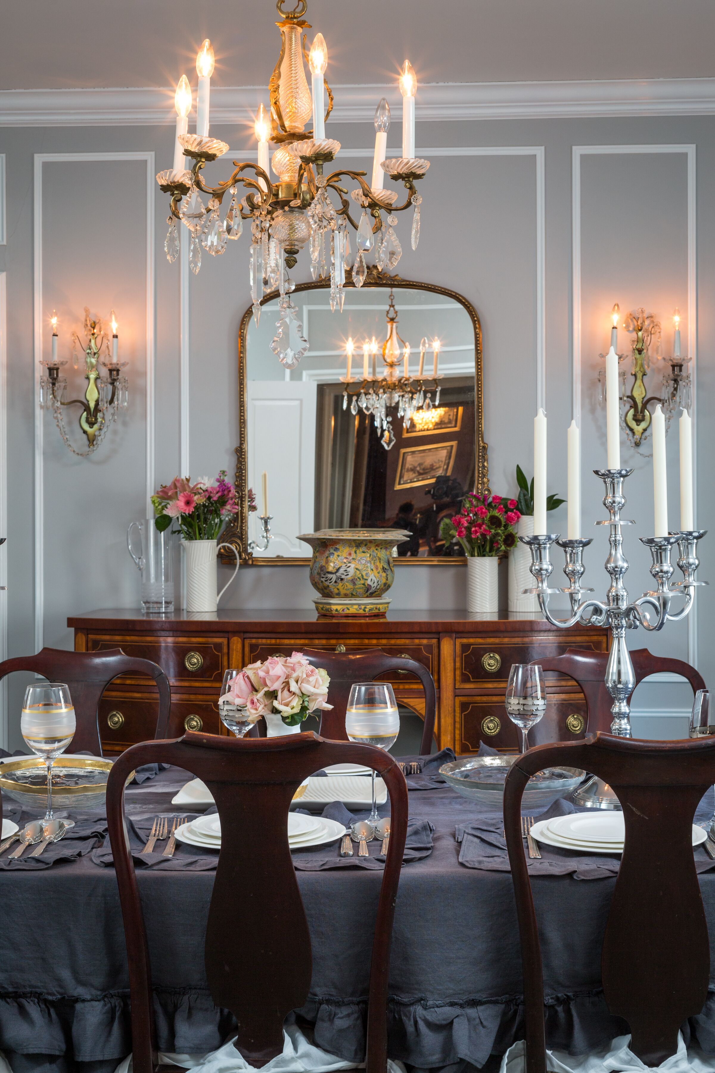 Un comedor formal con una araña, un espejo grande y una mesa puesta para la comida.