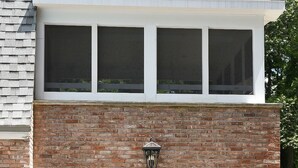 Ein Backsteinhaus mit einem großen Fenster und einer kleinen Außenbestuhlung mit Stühlen und einem Tisch.