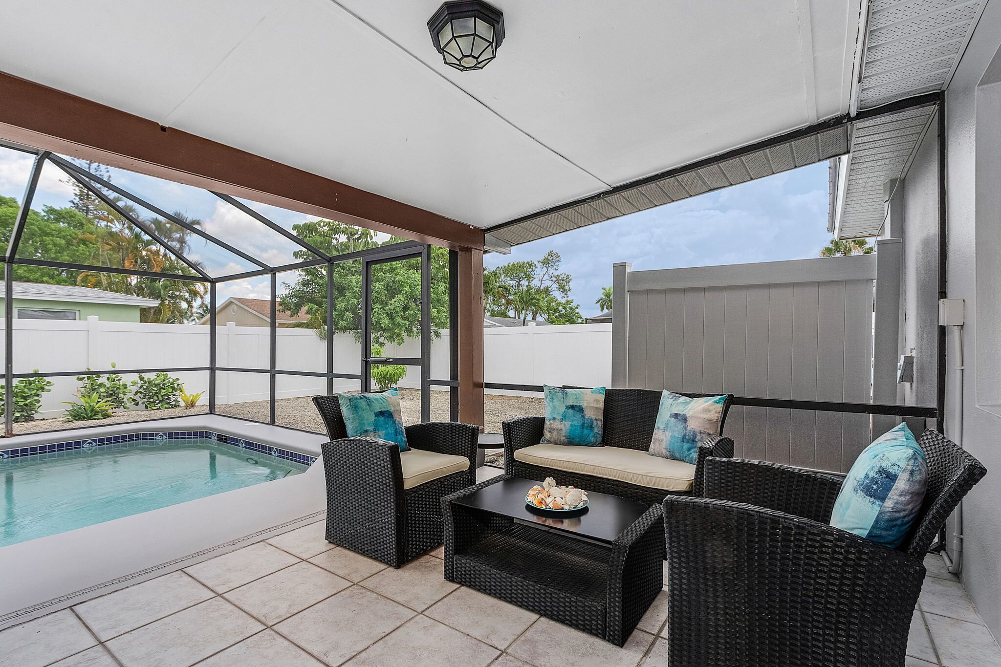 A covered patio with a pool, wicker furniture, and a view of the neighborhood.