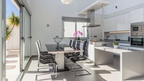 Una cocina moderna con una isla central, electrodomésticos integrados y un comedor con mesa de vidrio y sillas negras.